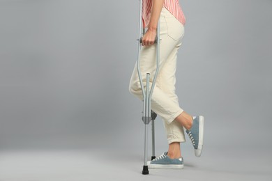 Photo of Young woman with axillary crutches on grey background, closeup. Space for text