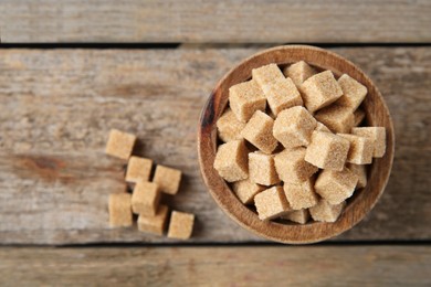 Photo of Bowl with brown sugar cubes on wooden table, top view