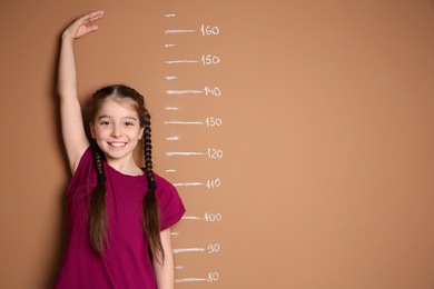 Little girl measuring her height on color background
