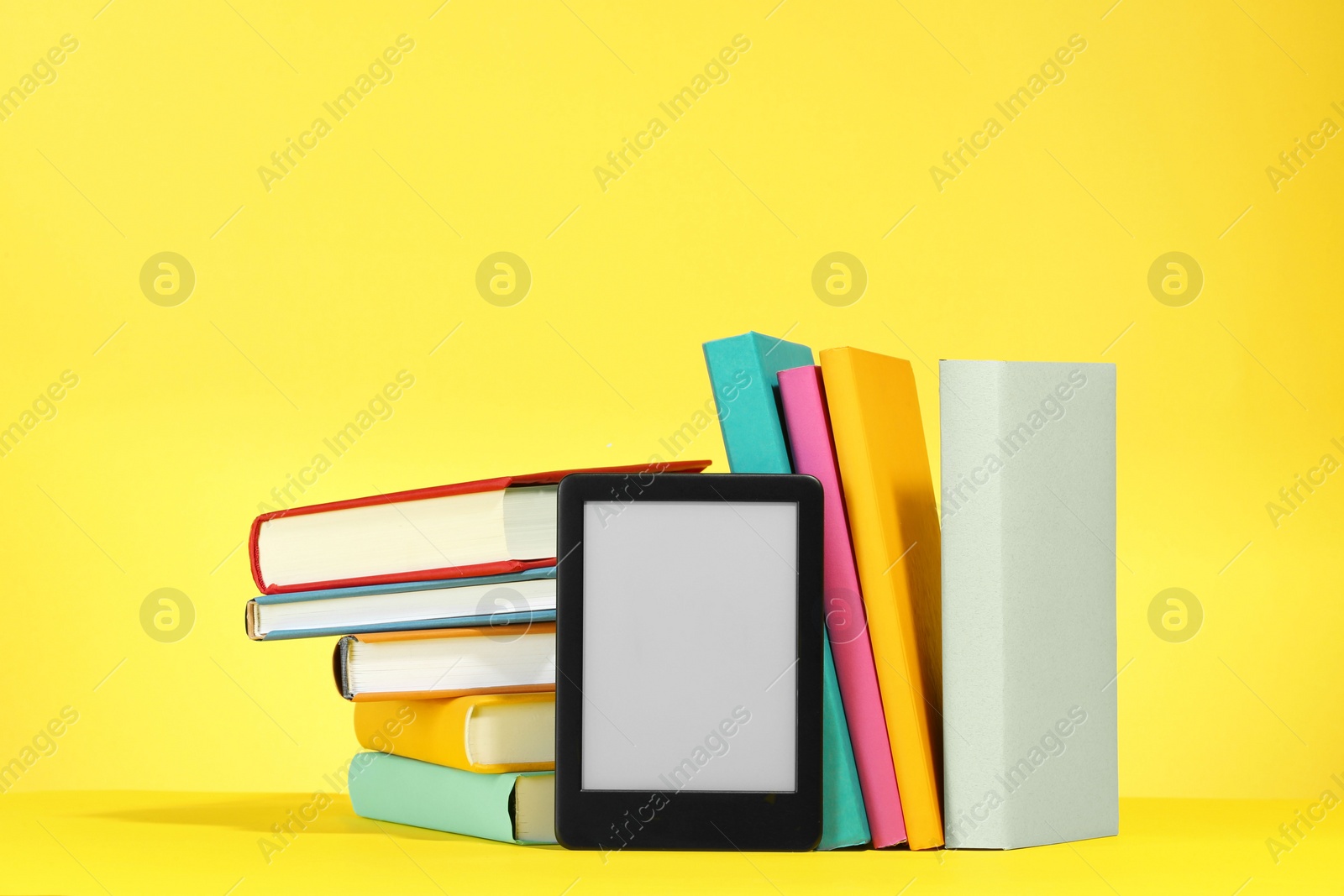 Photo of Modern e-book reader and hard cover books on yellow background