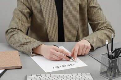 Photo of Woman filling Checklist at light grey table, closeup