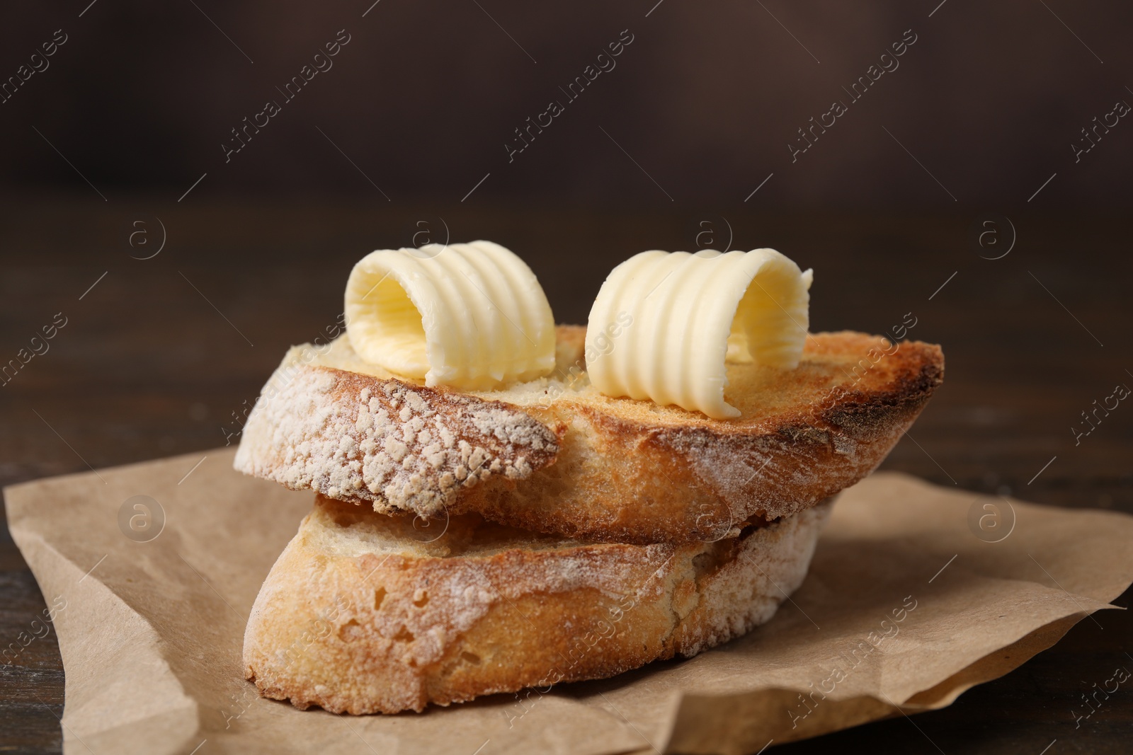 Photo of Tasty butter curls and slices of bread on wooden table, closeup