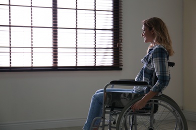 Young woman in wheelchair near window indoors