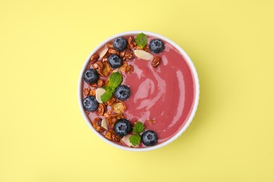 Bowl of delicious smoothie with fresh blueberries and granola on yellow background, top view