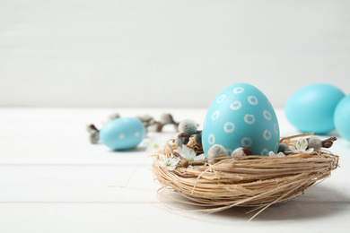 Photo of Colorful Easter egg in decorative nest on white wooden table. Space for text