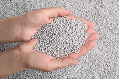 Photo of Woman holding chemical fertilizer over pellets, closeup. Gardening season