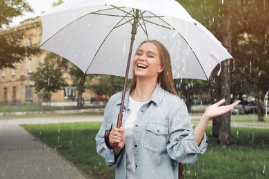 Young woman with umbrella walking under rain in park