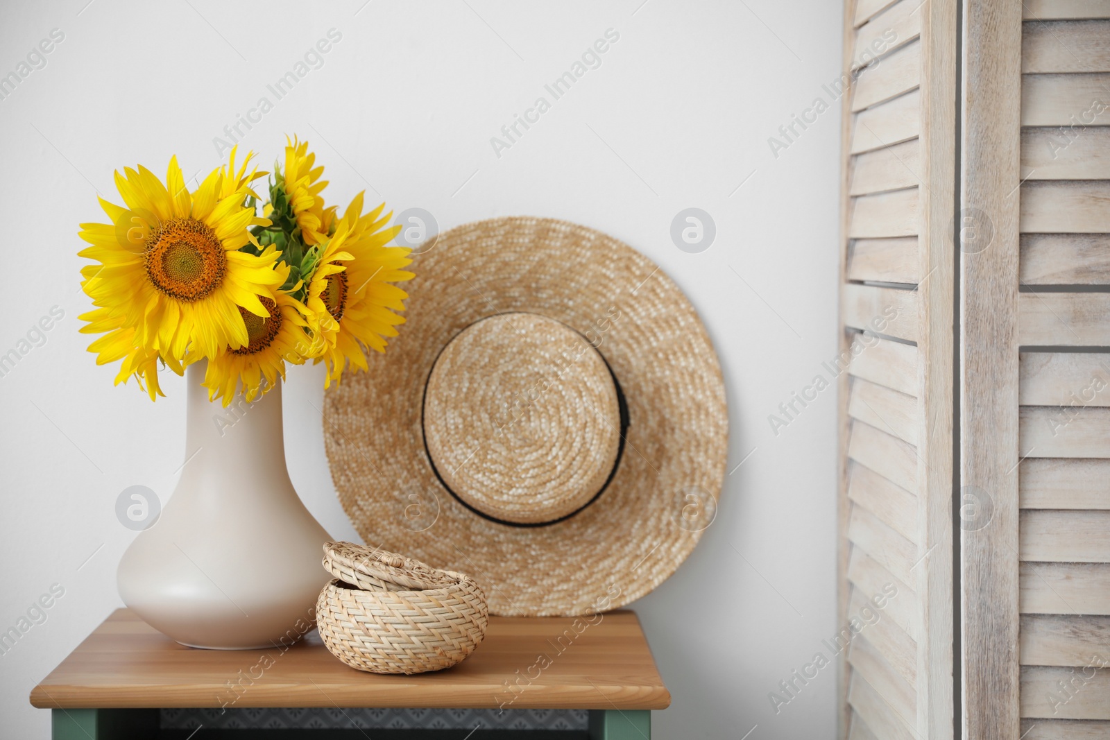 Photo of Bouquet of beautiful sunflowers, wicker basket and hat on table indoors