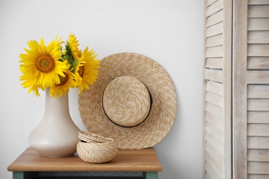 Photo of Bouquet of beautiful sunflowers, wicker basket and hat on table indoors