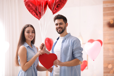 Lovely couple with heart shaped balloons in living room. Valentine's day celebration