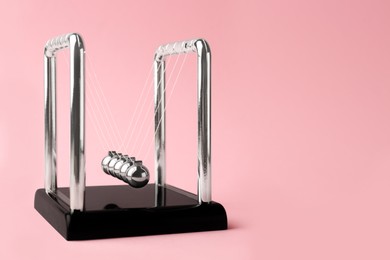 Photo of Newton's cradle on pink background, space for text. Physics law of energy conservation
