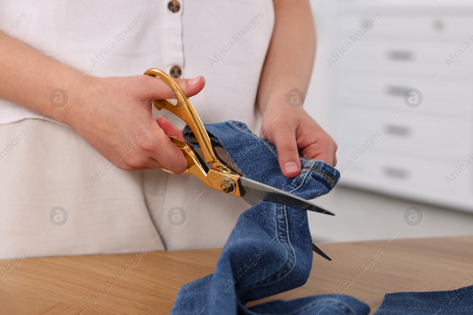 Photo of Woman cutting hem of jeans at table, closeup