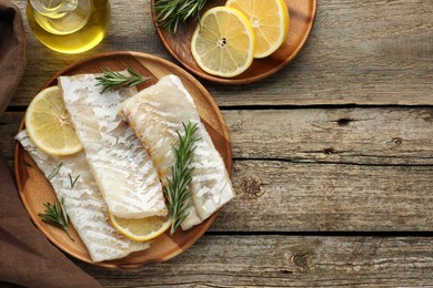 Photo of Fresh raw cod fillets with rosemary and lemon on wooden table, flat lay