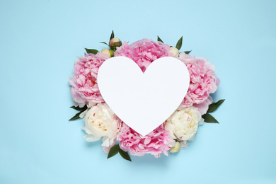 Photo of Beautiful peonies and blank heart shaped card on light blue background, flat lay. Space for text