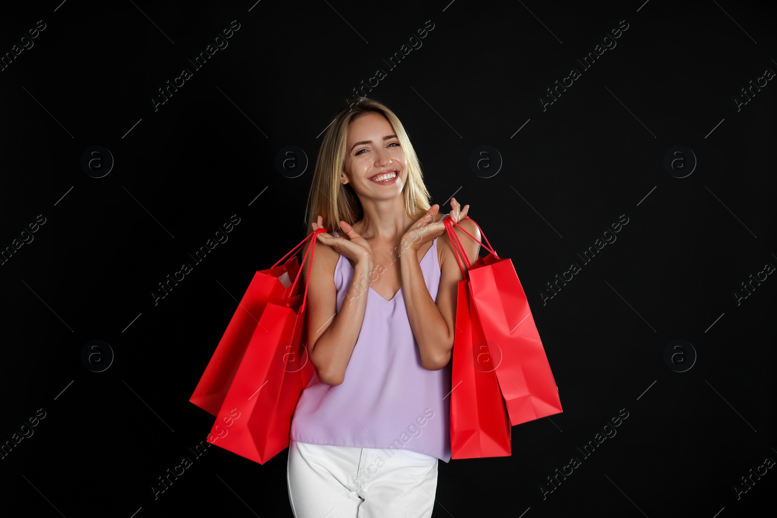 Photo of Happy young woman with shopping bags on dark background. Black Friday Sale