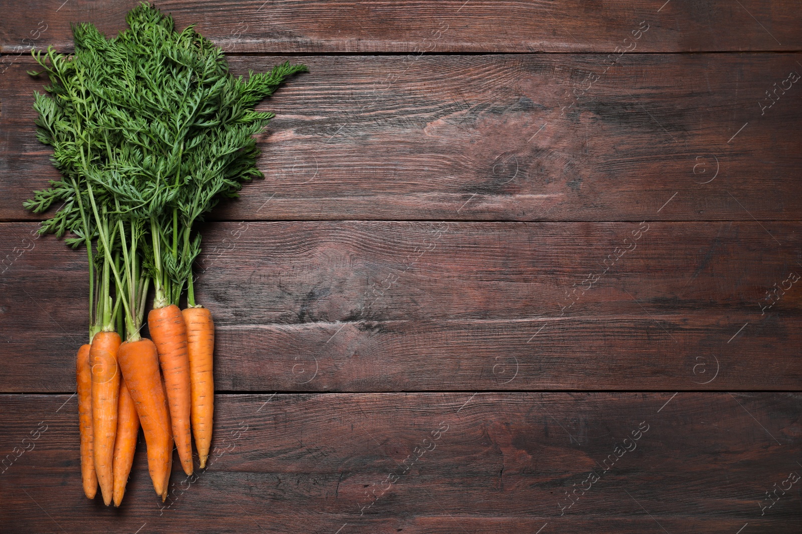 Photo of Ripe carrots on brown wooden table, flat lay. Space for text