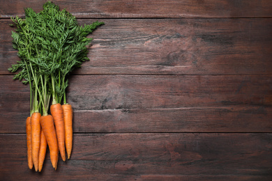 Ripe carrots on brown wooden table, flat lay. Space for text