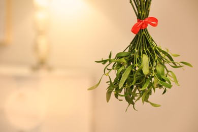 Photo of Mistletoe bunch with red bow on blurred background, space for text. Traditional Christmas decor