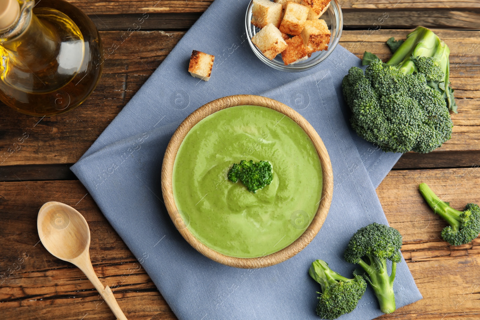 Photo of Delicious broccoli cream soup served on wooden table, flat lay