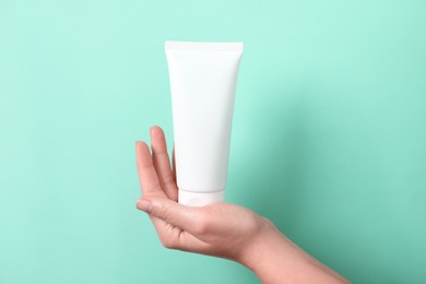 Photo of Woman with tube of hand cream on turquoise background, closeup