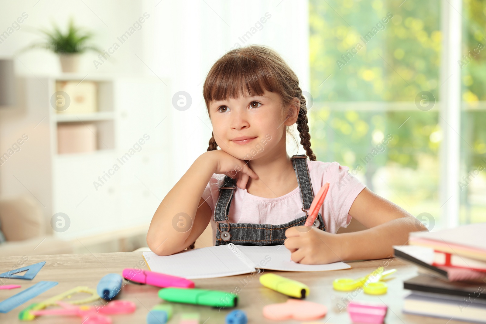 Photo of Cute girl doing homework at table with school stationery indoors