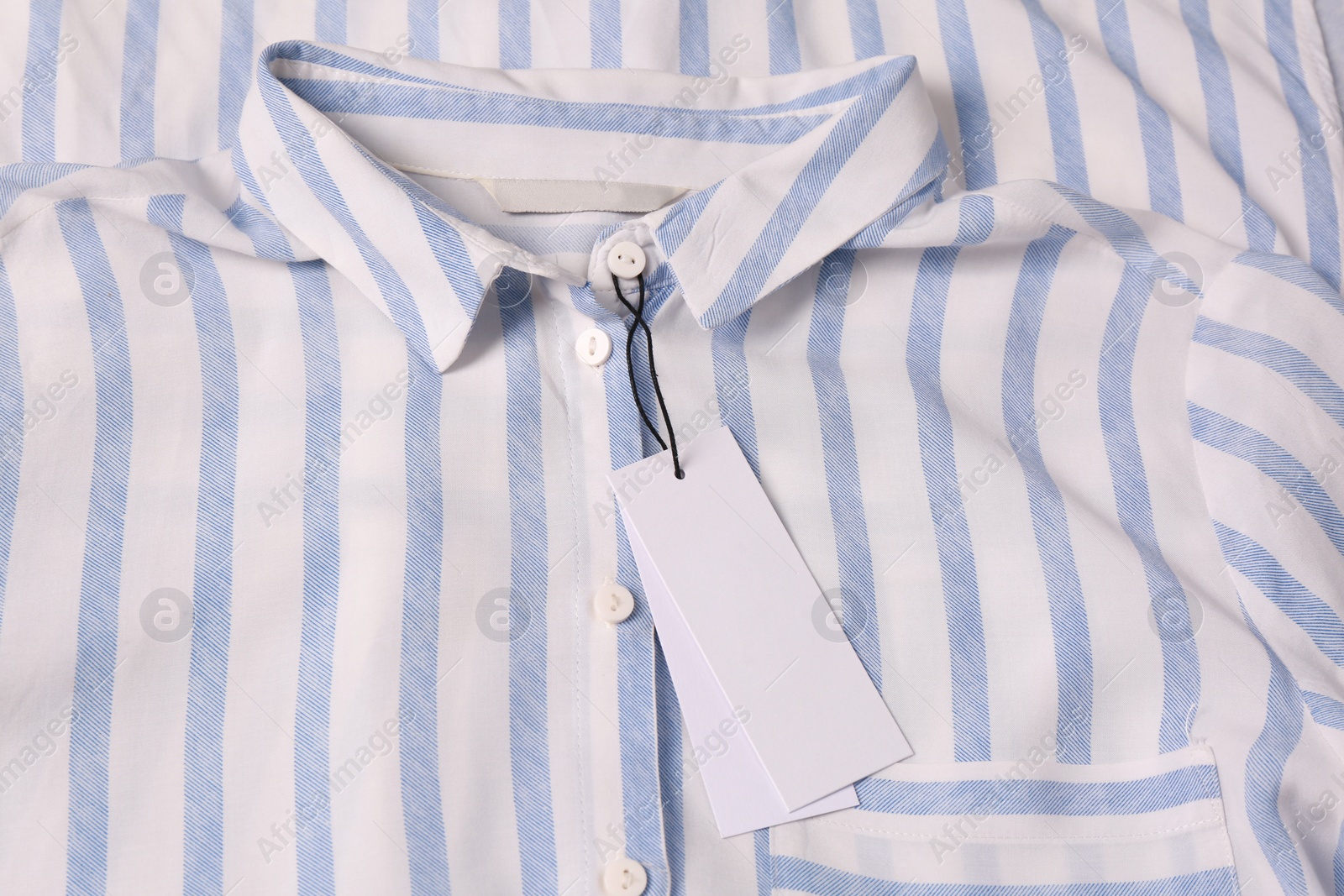 Photo of Blank white tags on striped shirt, top view. Space for text