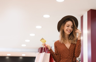 Photo of Happy young woman with shopping bags and credit card in mall