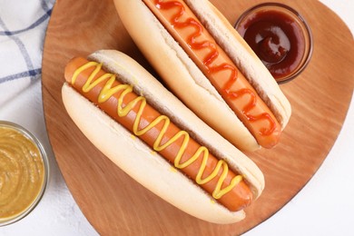 Tasty hot dogs with ketchup and mustard on white table, flat lay