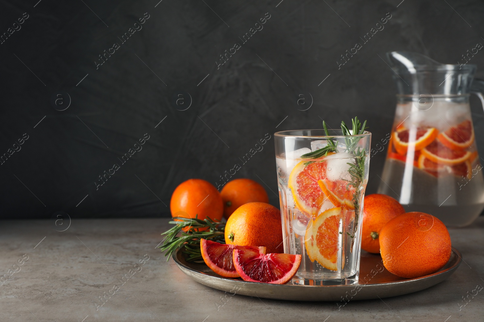 Photo of Delicious refreshing drink with sicilian orange and rosemary near fresh ingredients on grey table. Space for text