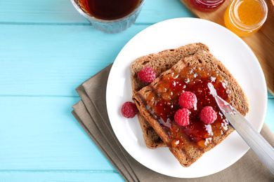 Tasty toast with raspberry jam and fresh berries for breakfast on turquoise table, flat lay