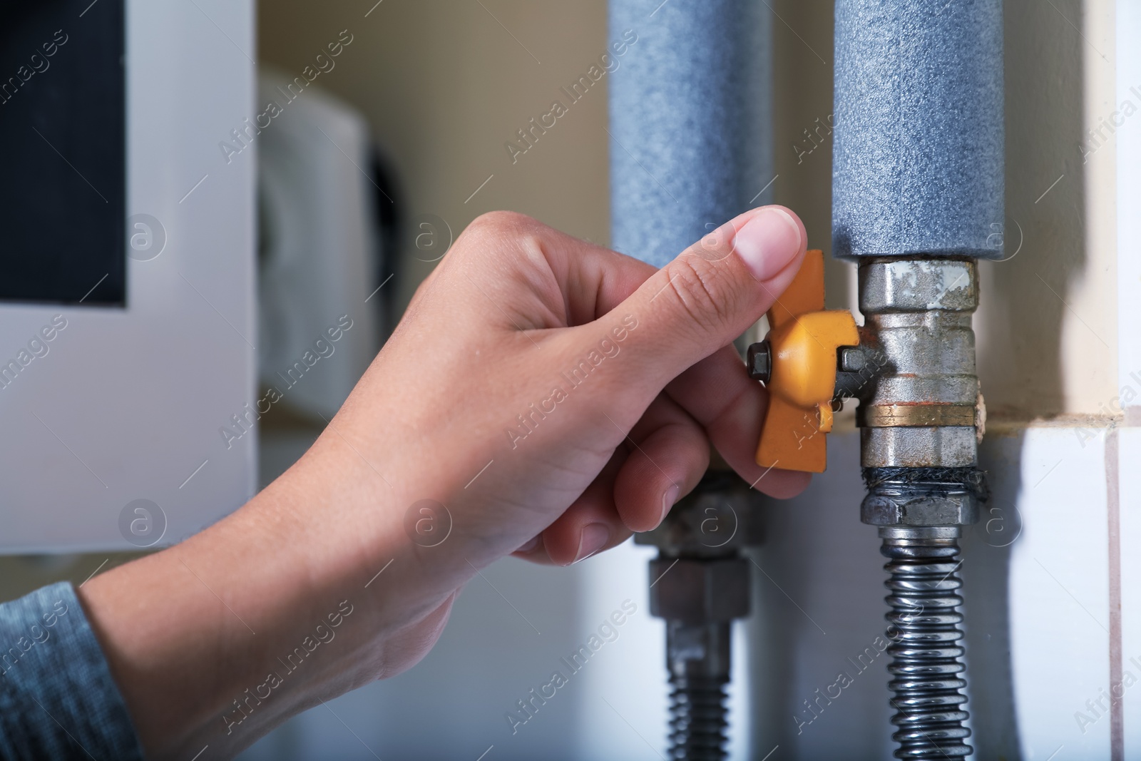 Photo of Woman turning on valve of gas boiler indoors, closeup