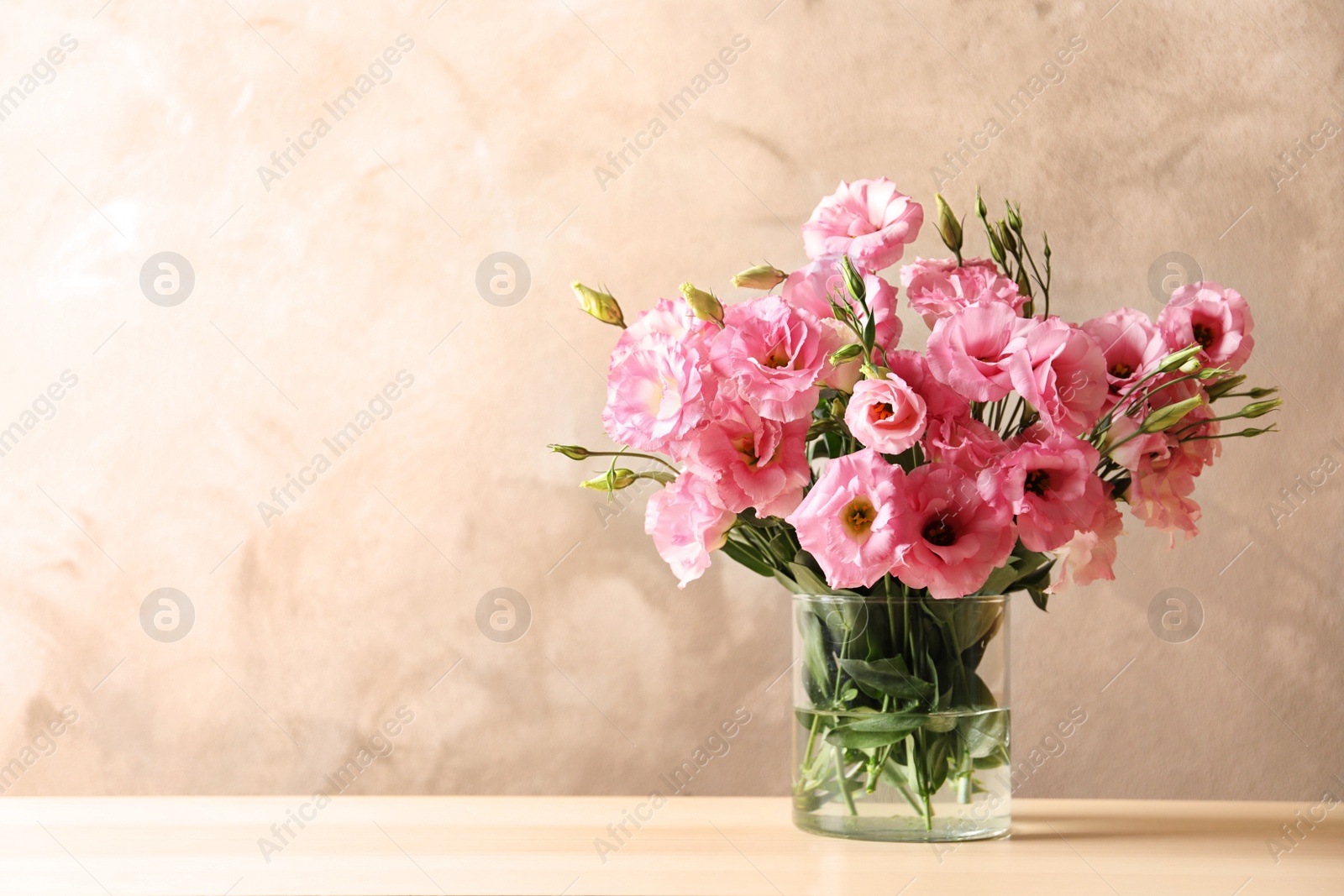 Photo of Vase with beautiful Eustoma flowers on table against color background