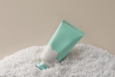 Winter skin care. Hand cream on artificial snow against light grey background