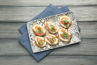 Photo of Tasty canapes with salmon, cucumber, cream cheese and dill on wooden table, top view