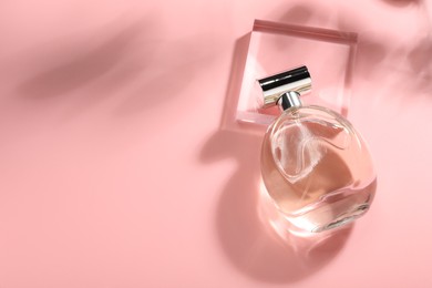 Bottle of luxury women's perfume in sunlight on pink background, above view. Space for text