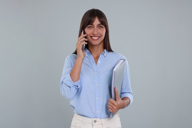Photo of Happy secretary with folder talking on smartphone against light grey background