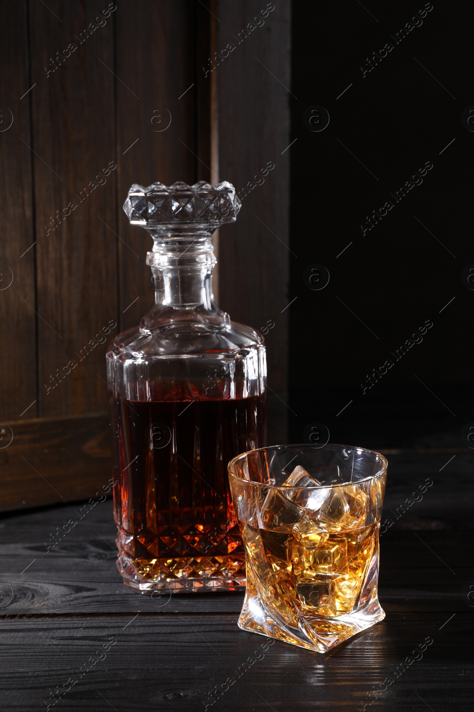 Photo of Whiskey with ice cubes in glass and bottle on black wooden table