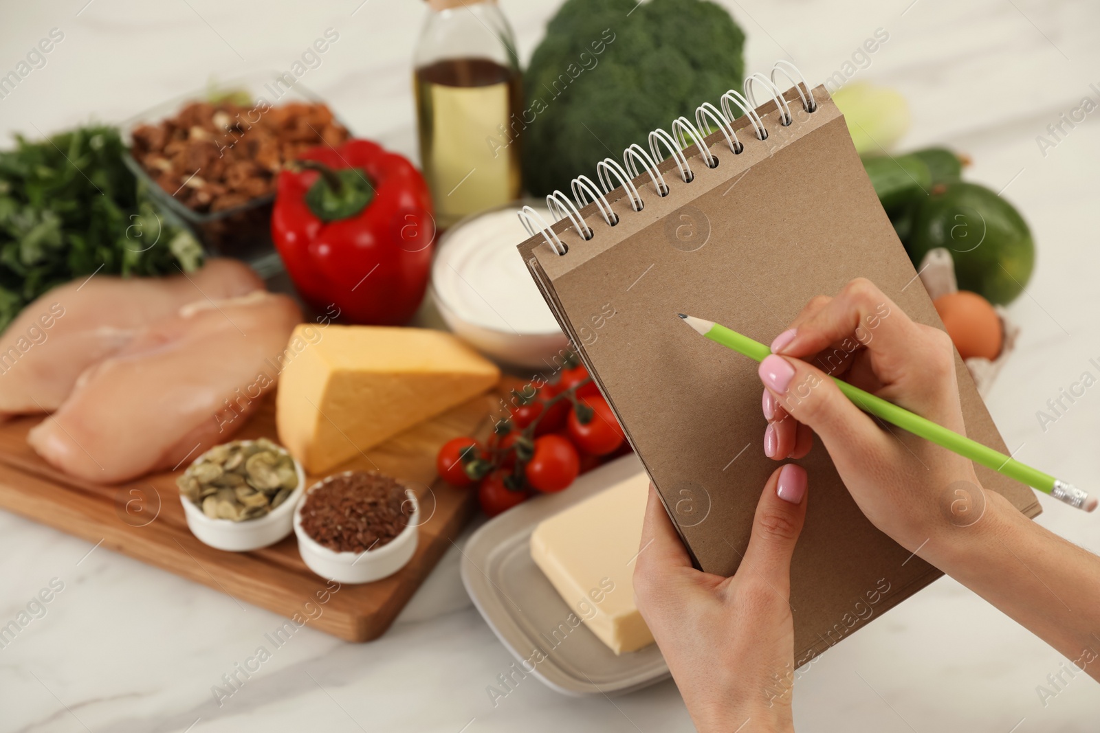 Photo of Woman writing in notebook near products at table, closeup. Keto diet