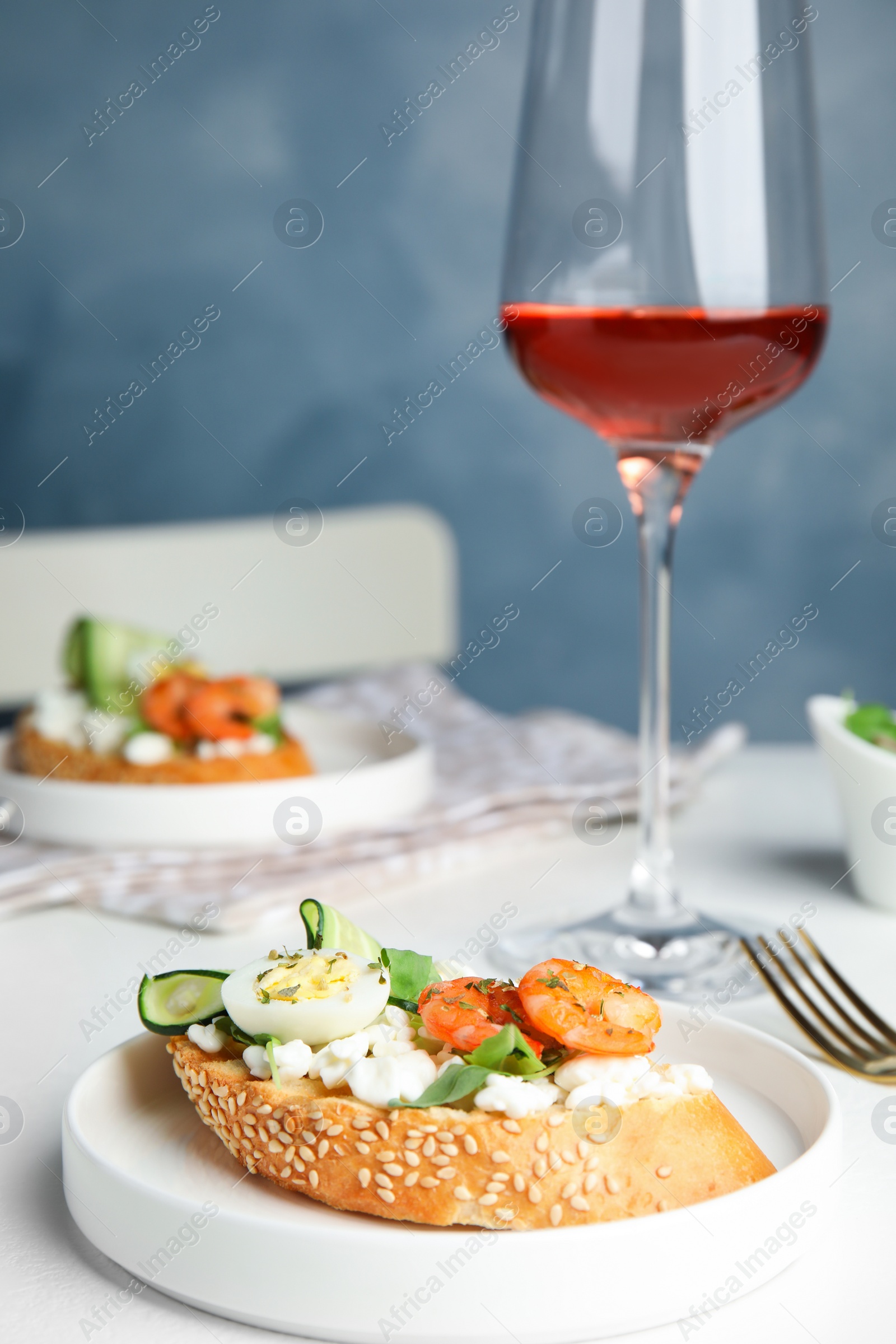 Photo of Delicious bruschetta with shrimps served on white table against blue background