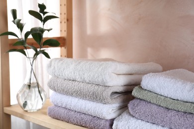 Photo of Stacked soft towels and green leaves on wooden shelf indoors