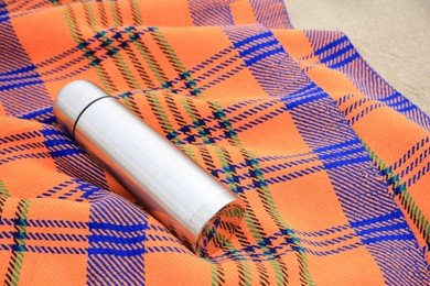 Metallic thermos with hot drink and plaid on sandy beach, space for text