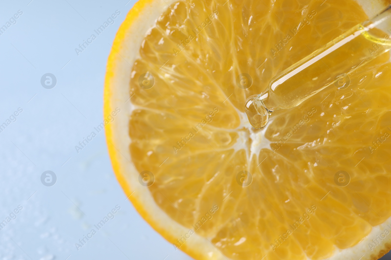 Photo of Dripping cosmetic serum from pipette onto orange slice against light blue background, top view