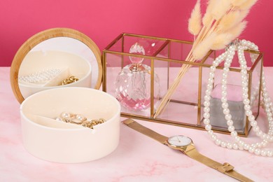 Jewelry box with many different golden accessories, perfume, wristwatch and dry flowers on pink marble table
