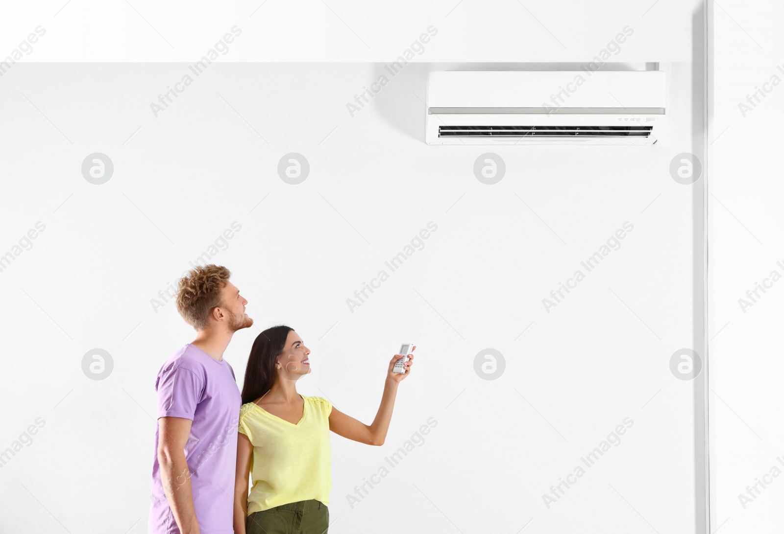 Photo of Young couple turning on air conditioner against white background