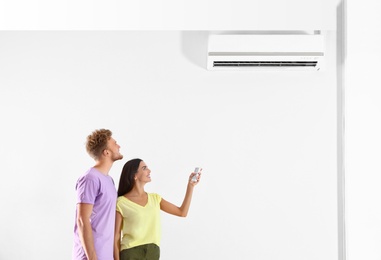 Photo of Young couple turning on air conditioner against white background