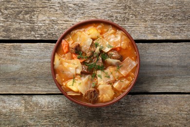 Photo of Tasty cabbage soup with meat, carrot and dill on wooden table, top view