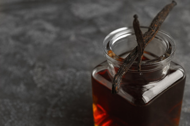 Photo of Aromatic homemade vanilla extract and dry pods on grey table, closeup. Space for text