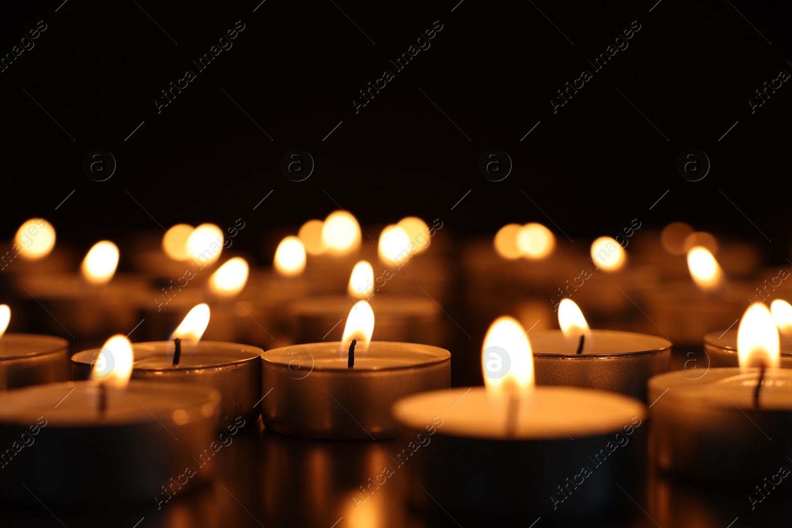 Photo of Burning candles on dark surface against black background, closeup