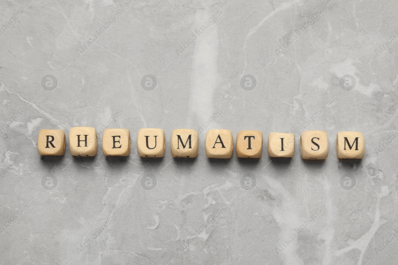 Photo of Word Rheumatism made of wooden cubes on light gray marble table, top view