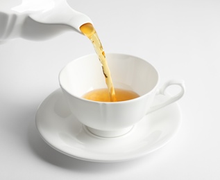 Photo of Pouring hot tea into porcelain cup on white background